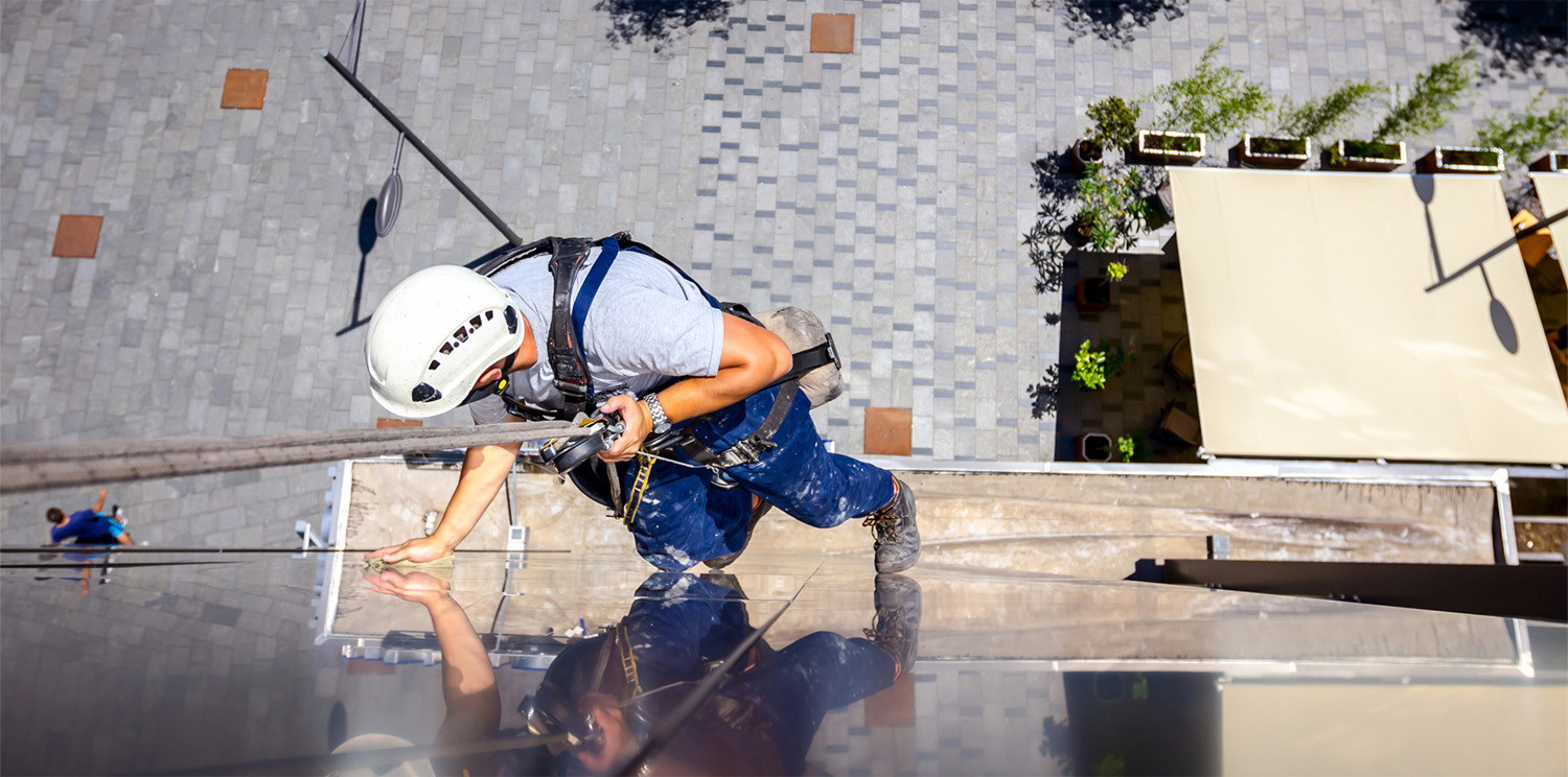 Above view on young man, industrial climber at work, he washing building facade.